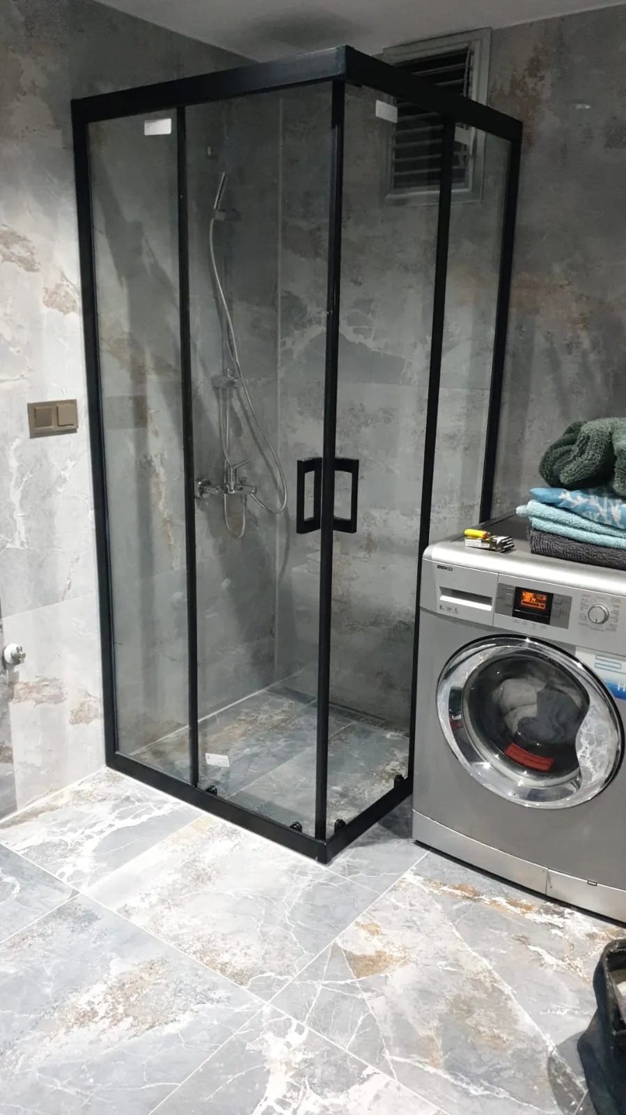 Siyah profilli köşe duşakabin, şeffaf temperli cam, gri mermer desenli banyo